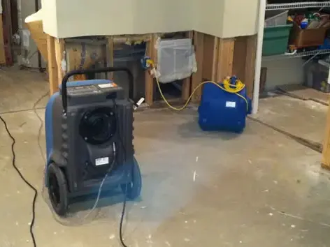Dehumidifier and air mover drying a room with the lower drywall cut away