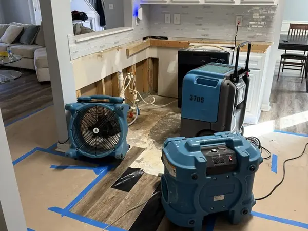 Air movers and a dehumidifier drying a kitchen with a section of flooring opened