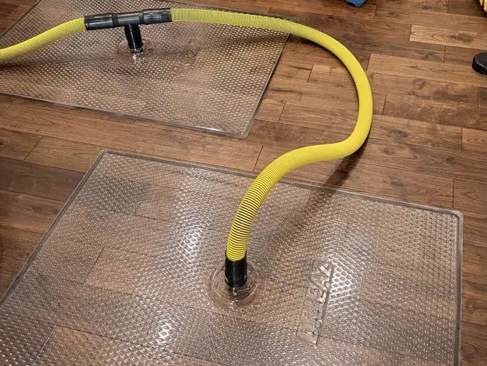 Floor drying mats and hoses pulling water out of wet hardwood planks
